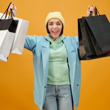 Smiling woman holding shopping bags against a bright yellow background, perfect for e-commerce and marketing.